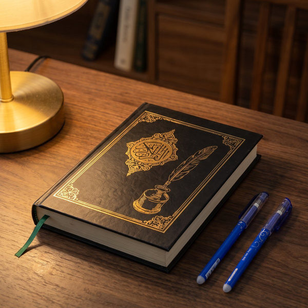 المصحف المظلل على مكتب ومعاه قلمين